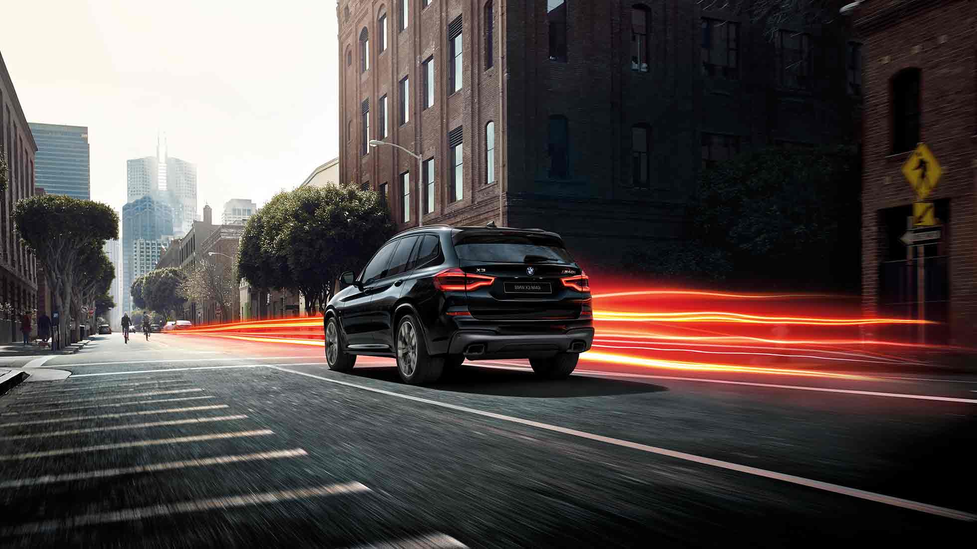 BMW X3 M40i, вид сзади с поворотом в три четверти. BMW X3 M40i, Черный Сапфир металлик, в движении, внешний вид, вид сзади с поворотом в три четверти на фоне городского пейзажа, полосы света.